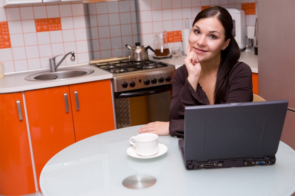 Young woman with laptop and coffee in her kitchen