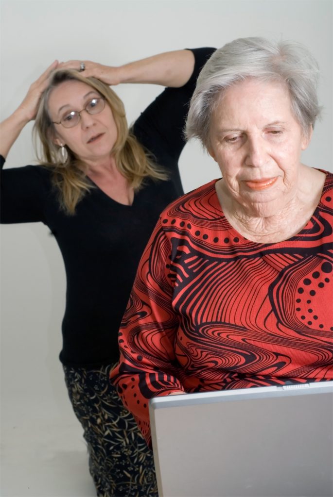 Woman looking over her elderly mother's shoulder while the older lady is working on a laptop