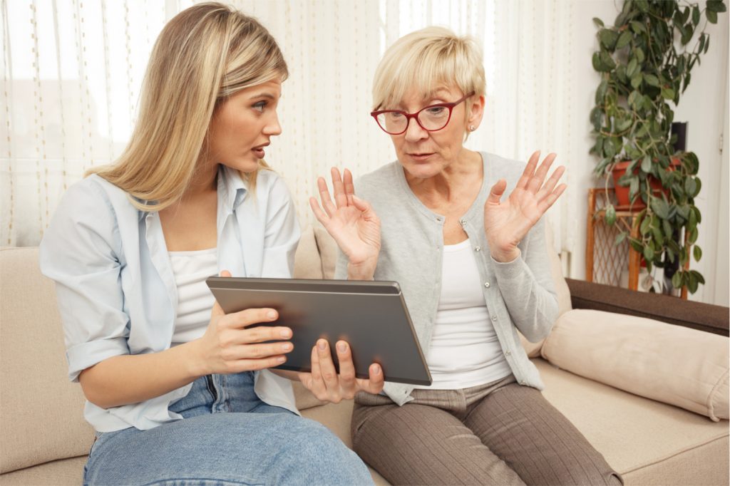Senior mother is getting annoyed while her daughter teaches her to use a tablet. 